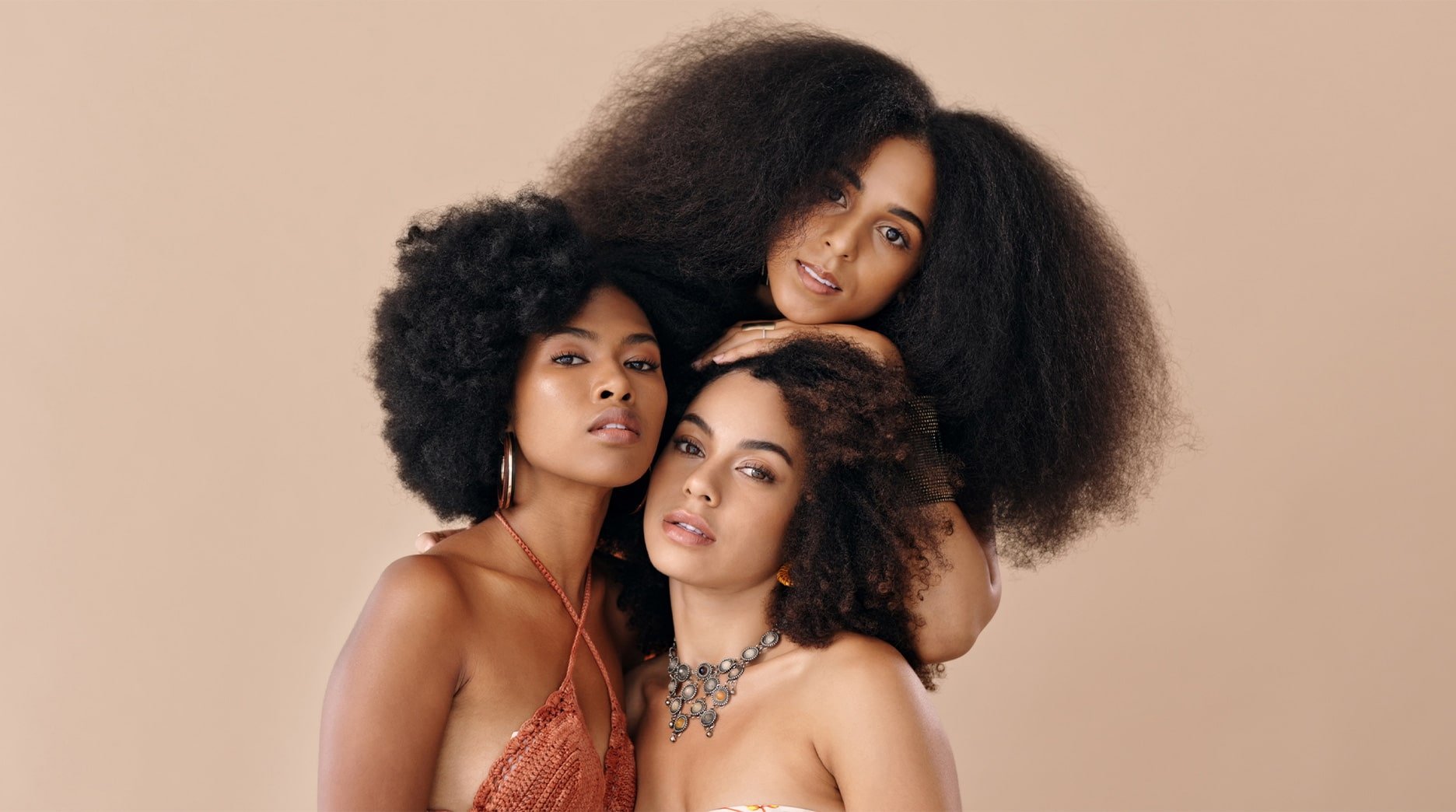 Three women with diverse skin tones and beautiful, voluminous curly hair styles stand together.